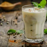 A refreshing cold yogurt drink served in a glass with ice, garnished with mint and spices.