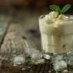 A refreshing cold yogurt drink in a glass, garnished with mint, served with ice cubes on a wooden table.